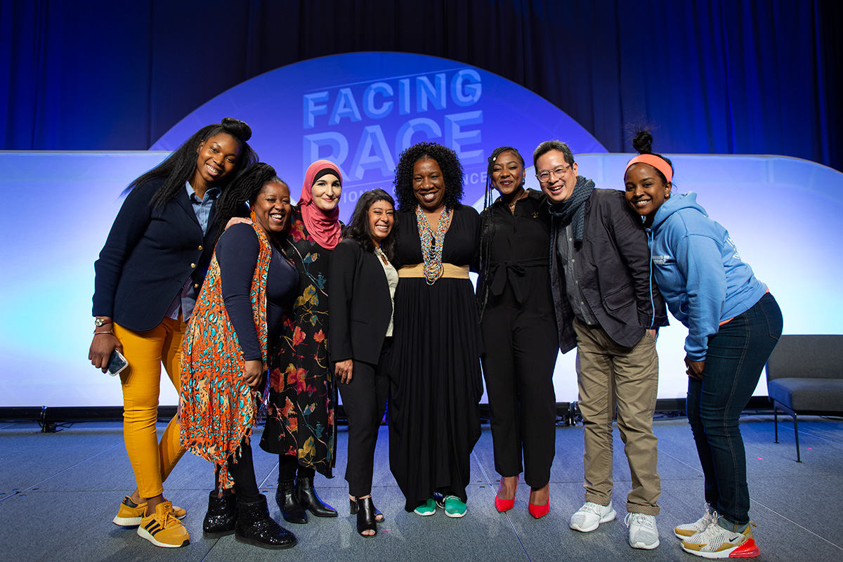 Eight people standing together on stage including Jeff Chang; Tarana Burke; Rinku Sen; and Alicia Garza