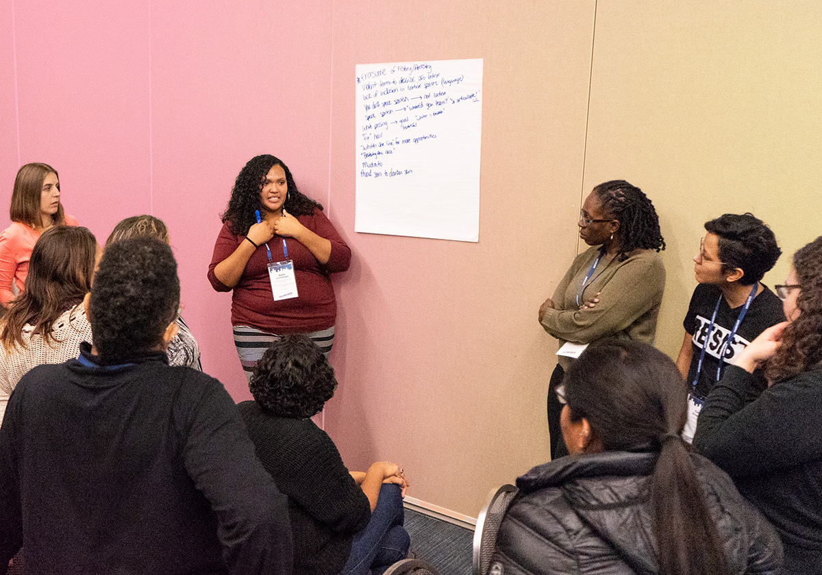 Several people standing and seated watching presenter.
