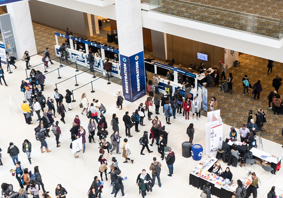 Crowed of people at conference registration and vendor tables.