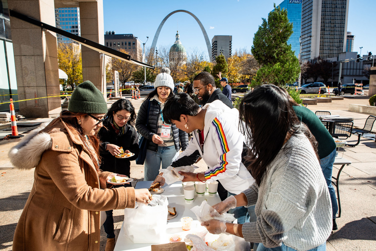 Folks gathering food oustside in St. Louis. The Gateway Arch is visible in the background.