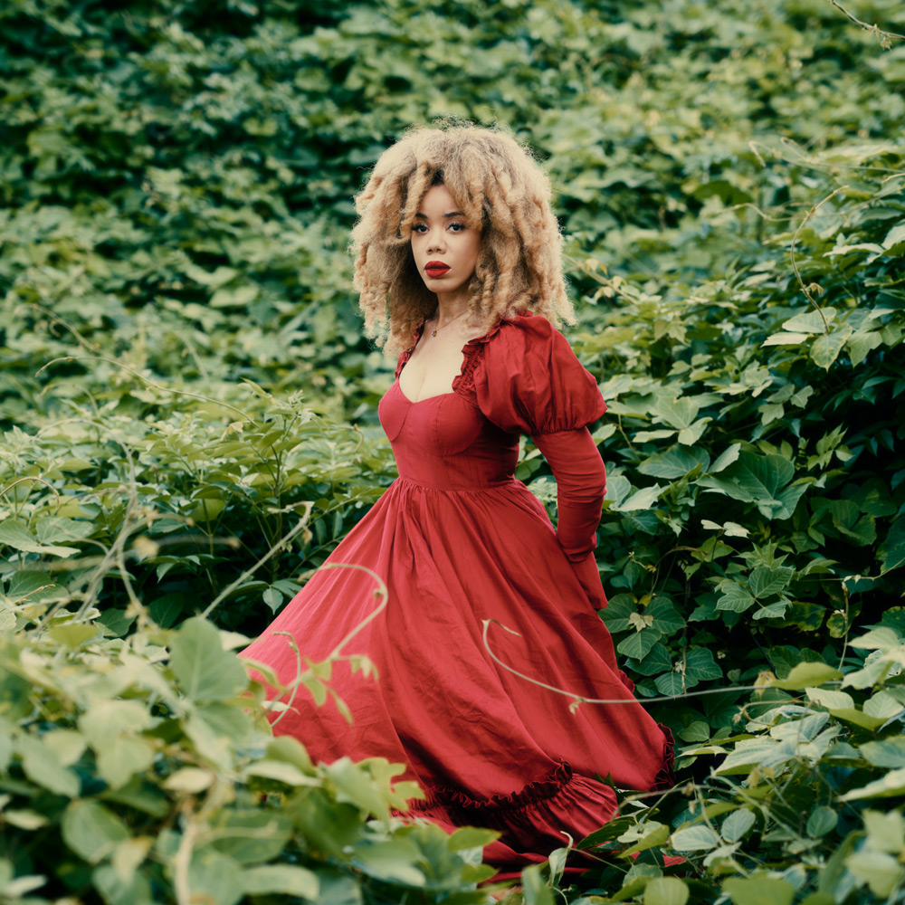 Kirby in a red dress standing amonst vining plants.