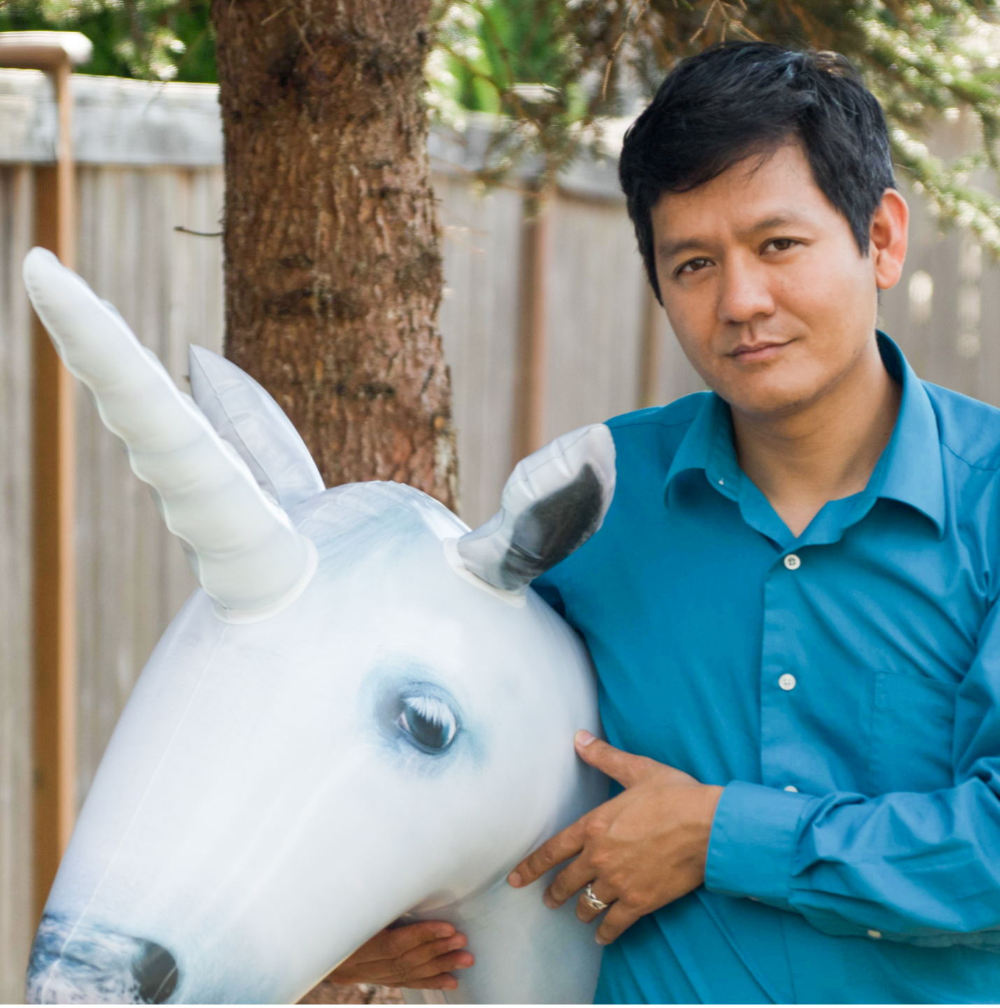 Photo of Vu Le in a blue shirt holding a stuffed unicorn animal