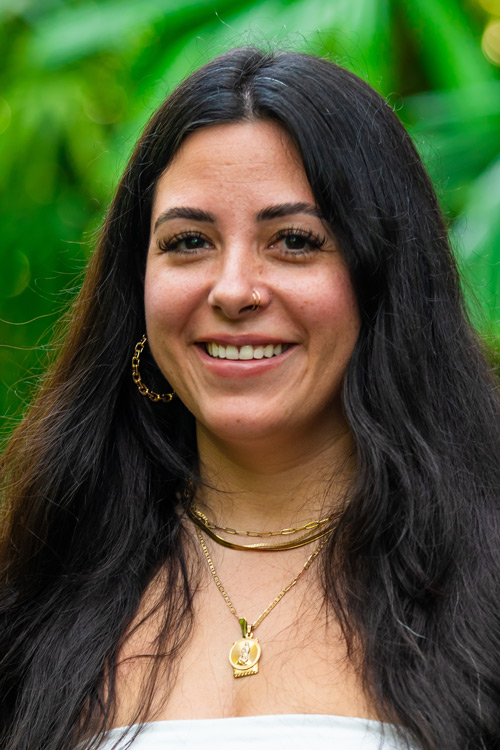 Smiling person standing in front of green plants.