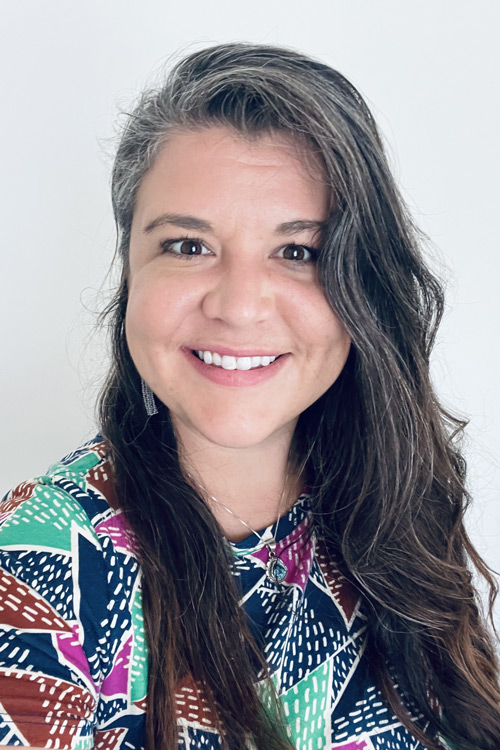 Person smiling in multi-color, patterned dress.