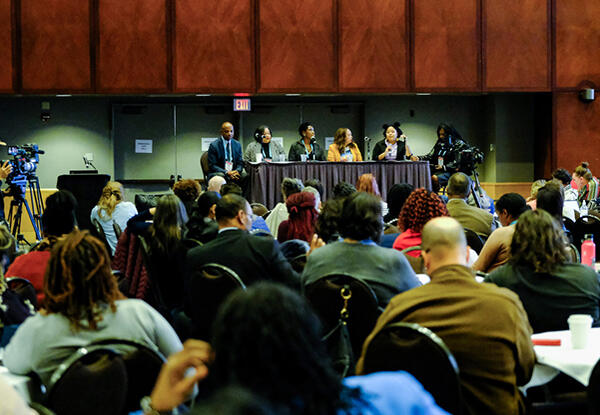 Audience looking on at speaker panel at table on stage.