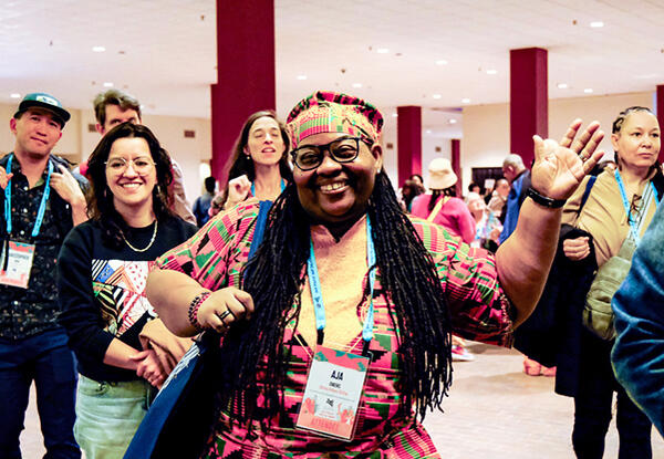 Smiling person waving with a group of other people.