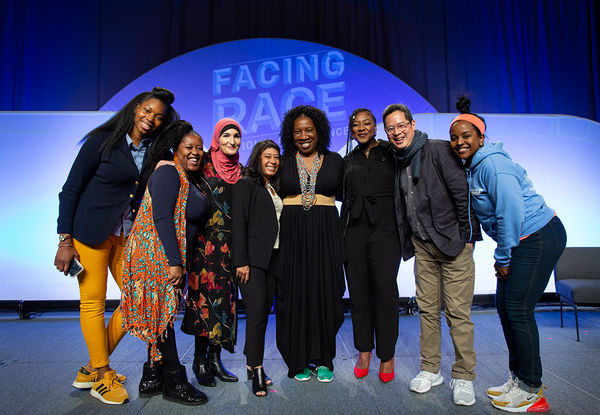 Eight people standing together on stage including Jeff Chang; Tarana Burke; Rinku Sen; and Alicia Garza