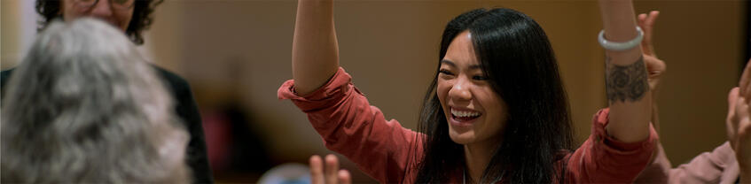 Smiling person in group with hands raised.