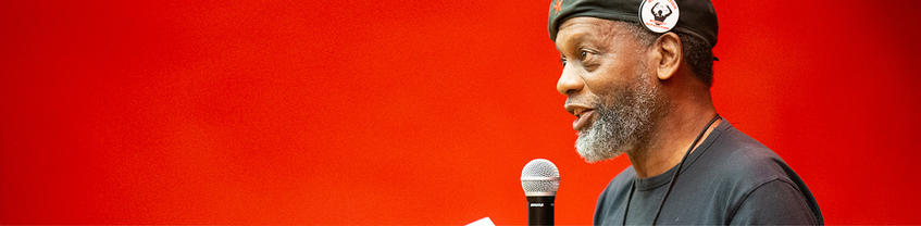 Person speaking into microphone with red background.