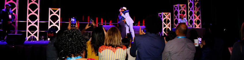 Two people hugging while standing on stage while people take photos or video with phones.