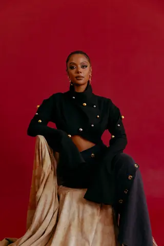 Herrana Addisu wearing black, seated on chair against a red background.