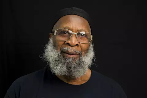photo of sekou with a kufi and silver beard and glasses on black background